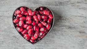 A heart shape container with pomegranate seeds.